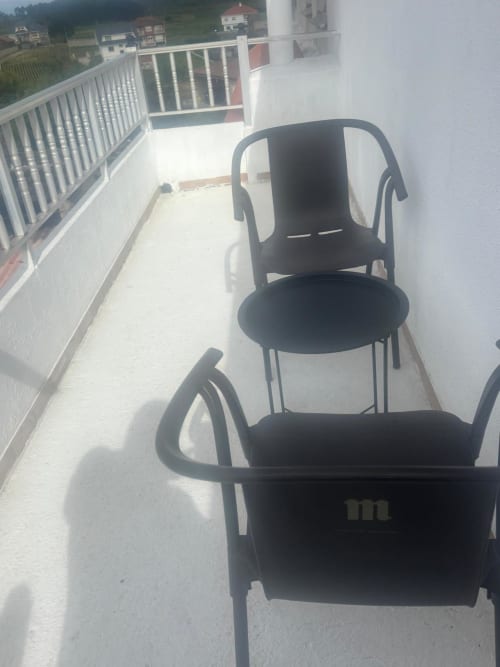Dos sillas negras en la terraza soleada del Hotel O Esqueiro en Malpica, A Coruña, con vistas al pueblo de montaña