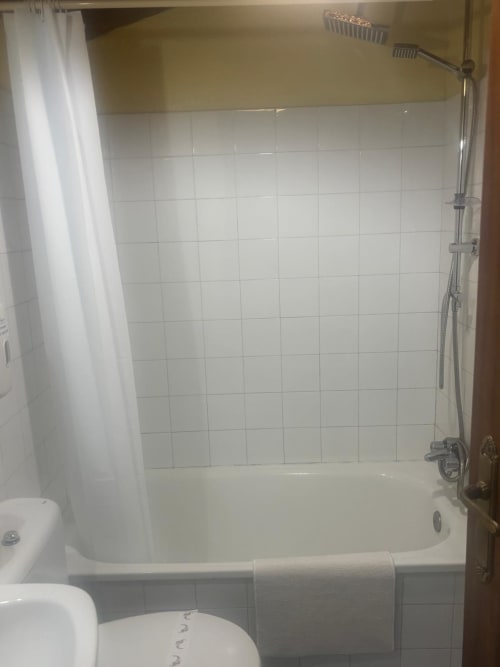 Baño limpio con azulejos blancos y bañera en el Hotel O Esqueiro en Malpica, A Coruña