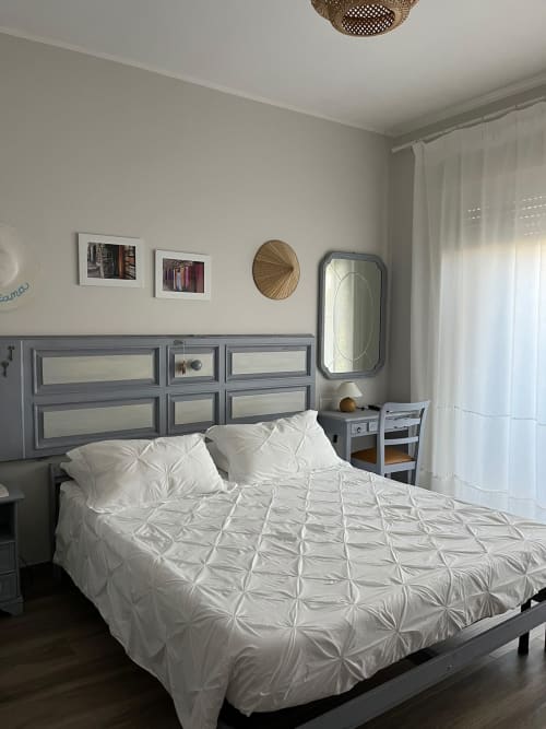 Camera moderna di Maison Tizi con piumone bianco plissettato, testiera grigia, specchio e tende leggere a Fiumicino Roma