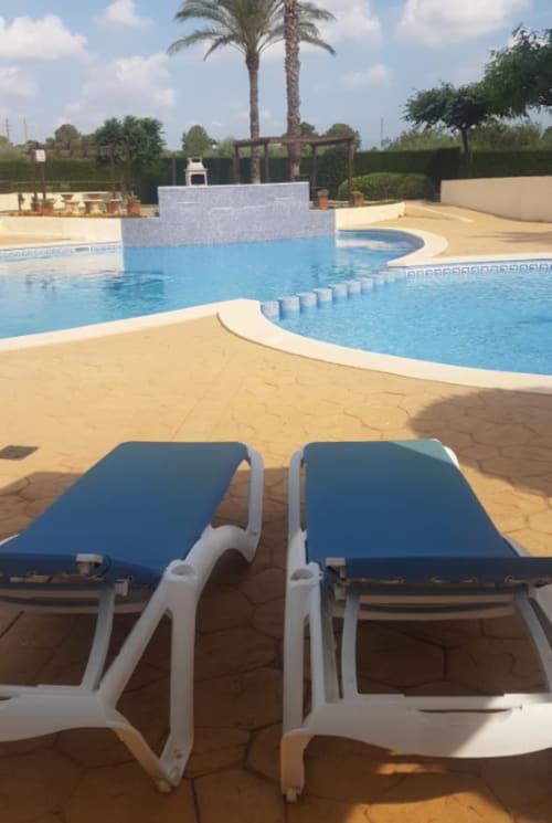 Dos tumbonas azules en la terraza soleada con vistas a la piscina y palmeras en Olivos del Sol, Sant Jordi