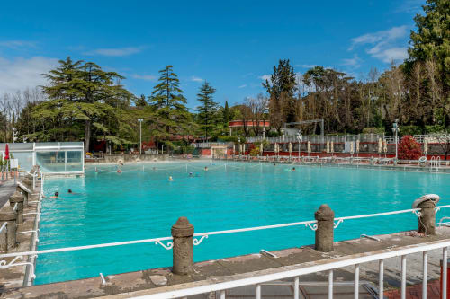 Piscina turchese presso MAISON TIZI a Fiumicino Roma con lettini, alberi e cielo sereno