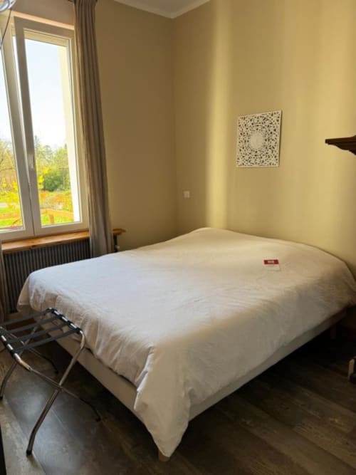 Chambre lumineuse à Au Bois Dormant avec lit blanc, grande fenêtre sur le jardin, murs crème et décoration moderne.