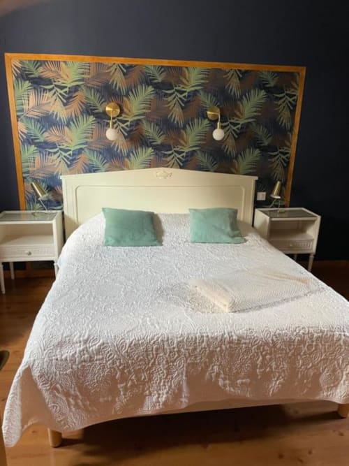 Chambre moderne à Au Bois Dormant avec lit crème, oreillers verts, tête de lit tropicale et tables de nuit en bois
