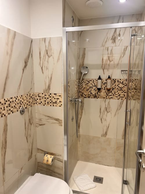 Bagno moderno dell'Hotel Ercoli House Roma con piastrelle effetto marmo, fascia mosaico decorativa, box doccia in vetro e finiture bianche