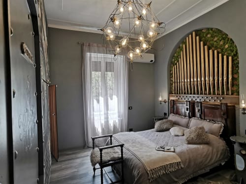 Luxury bedroom at The Kraken Inn, Bergamo with ornate headboard, geometric chandelier, and decorative moss wall accent.