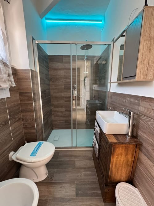 Bagno moderno nell'appartamento Victoria del Queen Hotel, Campofilone con piastrelle effetto legno, doccia in vetro e dettagli turchesi