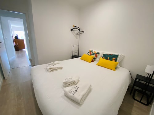 Quarto luminoso na Casa das 7 Janelas em Peniche com cama branca, almofadas amarelas e vista para a cidade