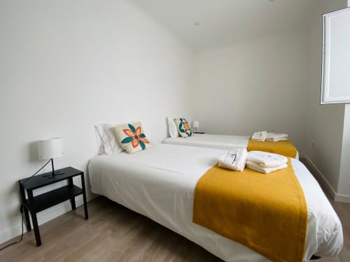 Quarto luminoso na Casa das 7 Janelas em Peniche com cama branca, almofadas coloridas e manta amarelo mostarda