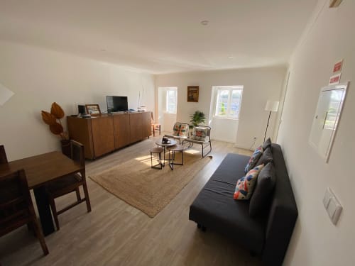 Sala de estar luminosa com sofá preto, móveis em madeira e janelas na Casa das 7 Janelas em Peniche