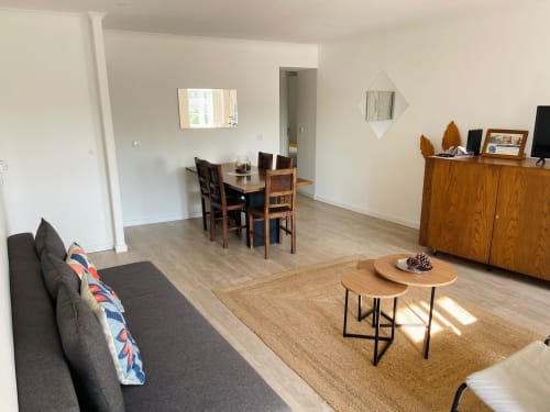Sala de estar moderna em apartamento da Casa das 7 Janelas em Peniche com mesa de jantar, sofá, móveis em madeira e vista para a cidade