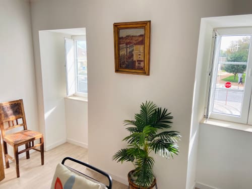 Interior luminoso do Casa das 7 Janelas em Peniche com cadeira de madeira, planta em vaso e quadro com arte urbana em parede branca