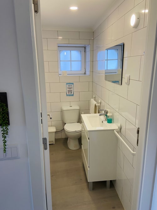 Casa das 7 Janelas em Peniche: banheiro moderno com azulejos brancos, pia, vaso sanitário e box de chuveiro