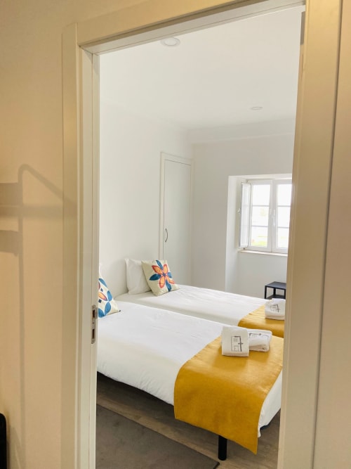 Duas camas individuais com manta amarela na Casa das 7 Janelas, apartamento em Peniche com vista para a cidade e comodidades modernas