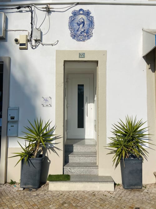 Entrada do apartamento Casa das 7 Janelas em Peniche com azulejos portugueses azuis, plantas em vasos e número da casa 22