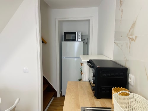 Cozinha compacta em Casa das 7 Janelas em Peniche com micro-ondas, geladeira, forno preto e bancada de madeira