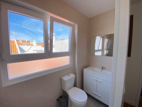 Banheiro moderno na Casa das 7 Janelas com acabamentos brancos e vista da cidade de Peniche, Portugal pela janela