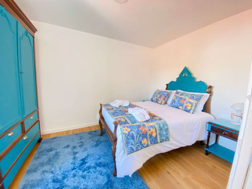 Quarto luminoso da Casa das 7 Janelas em Peniche com cabeceira turquesa, roupa de cama estampada, tapete azul e piso de madeira
