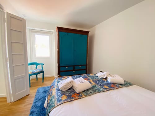 Quarto luminoso na Casa das 7 Janelas em Peniche com cama, guarda-roupa verde-azulado, cadeira azul e assoalho em madeira
