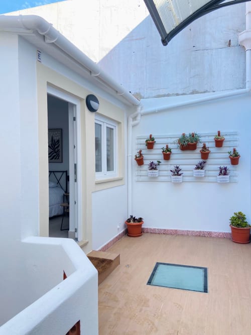 Terraço ensolarado da Casa das 7 Janelas em Peniche com plantas em vasos, paredes brancas e piso de madeira
