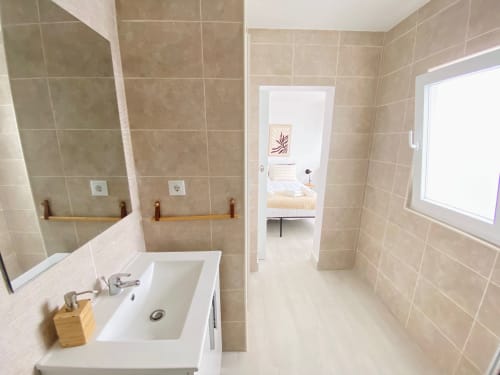 Banheiro moderno da pousada Casa das 7 Janelas em Peniche com azulejos bege, pia, espelho e vista para o quarto