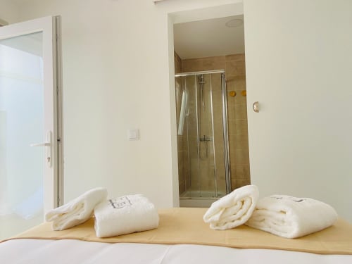 Quarto com toalhas brancas dobradas e roupões na cama, banheiro privativo com box de vidro na Casa das 7 Janelas