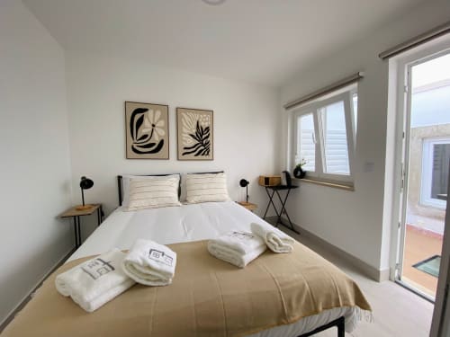 Quarto moderno da Casa das 7 Janelas em Peniche com linens brancos, cabeceira escura e vista para o oceano através de portas de vidro