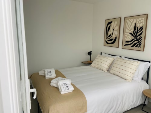 Quarto moderno da Casa das 7 Janelas em Peniche com roupa de cama branca, almofadas às riscas e arte botânica na parede