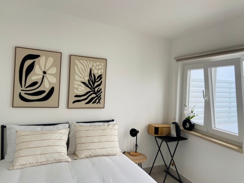 Quarto luminoso da Casa das 7 Janelas em Peniche com roupa de cama branca, arte botânica na parede e vistas para o oceano