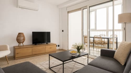Sala de estar moderna con vista al mar en Holidays Costa Brava, TV, sofá gris, muebles de madera y acceso a balcón
