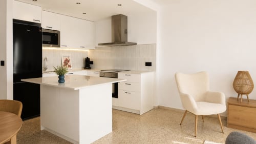 Cocina y salón de planta abierta moderna en apartamento Holiday Manhattan, Empuriabrava, con muebles blancos, isla y vistas al mar
