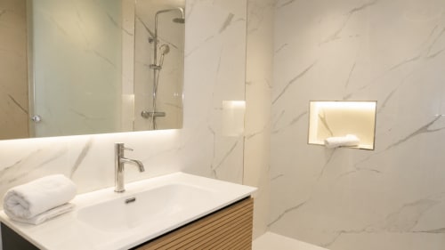 Baño moderno en Holidays Costa Brava con paredes de mármol, lavabo blanco, espejo y accesorios de ducha