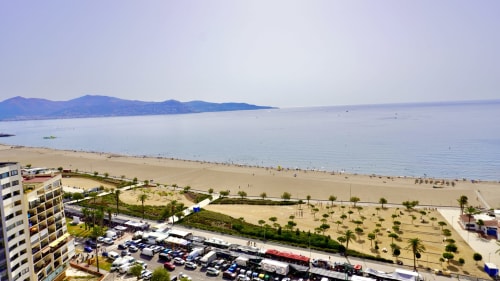 Playa de Empuriabrava con aguas azules del Mediterráneo, arena dorada y montañas al fondo desde el balcón del hotel Holidays Costa Brava