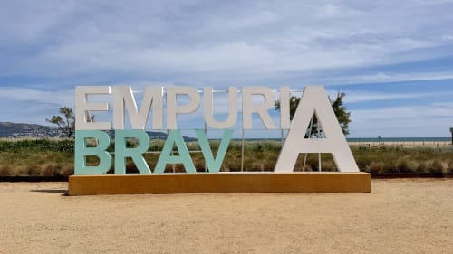 Letrero de bienvenida a Empuriabrava con paisaje costero, puerta de entrada a los apartamentos Holidays Costa Brava en España