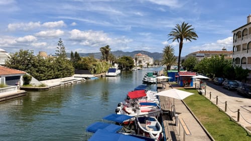Marina de Empuriabrava con barcos amarrados, palmeras y edificios frente al mar bajo cielo azul