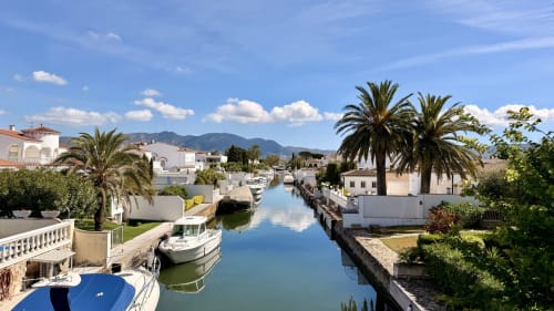 Vista tranquila del canal en Empuriabrava con villas blancas frente al agua, palmeras y barcos amarrados bajo cielo azul