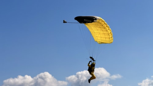 Paracaidista con paracaídas amarillo descendiendo sobre la costa de Empuriabrava con nubes blancas y cielo azul