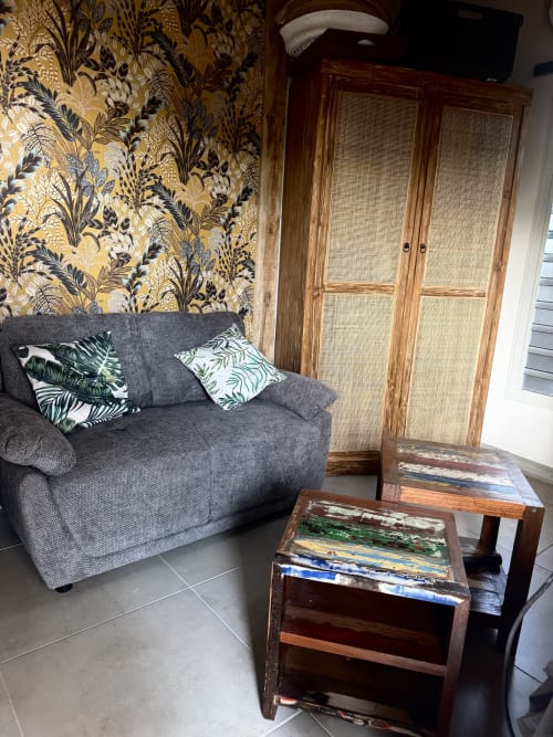 Salon cozy de l'appartement Bielle, Tiki Kaz à Saint François avec canapé gris, papier peint à motifs et mobilier en bois.