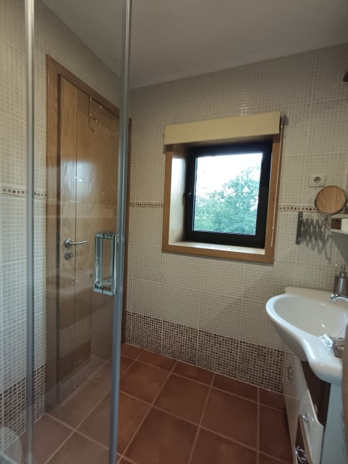 Banheiro moderno com duche aberto, lavatório suspenso e janela com moldura de madeira na Quinta d'Areda Wine&Pool Experience