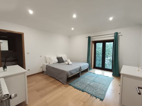 Quarto duplo luminoso na Quinta d'Areda com duas camas, cortinas verdes, portas com vista para o lago e comodidades modernas em Fafe