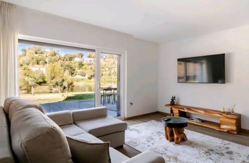 Sala de estar moderna da Casa Carvalho em Serração House Gerês com vista para o rio, sofá bege, móveis de madeira e amplas janelas