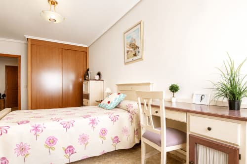 Dormitorio luminoso en el apartamento Quintanes de Riurau Home, Calp, con ropa de cama floral, armario de madera y muebles color crema
