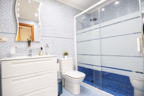 Baño moderno en Riurau Home, Calp con azulejos mosaico azules, tocador blanco, inodoro y ducha de cristal