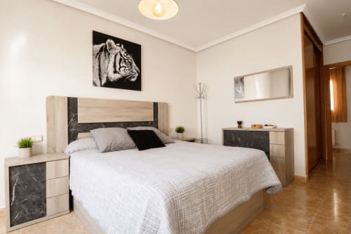 Dormitorio moderno en apartamento Riurau Home de Calp con cama de madera, detalles en mármol oscuro, ropa de cama blanca y arte de tigres