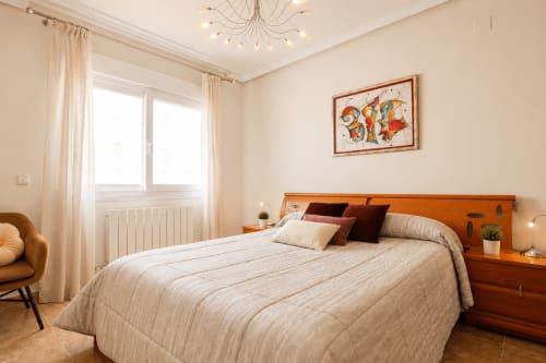 Dormitorio luminoso en apartamento Riurau Home Calp con cama de madera, ropa de cama color crema y equipamientos modernos