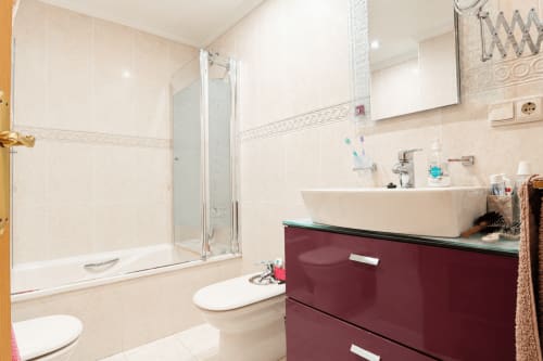 Baño moderno en apartamento Quintanes de Riurau Home, Calp, con tocador burdeos, lavamanos blanco y ducha de cristal