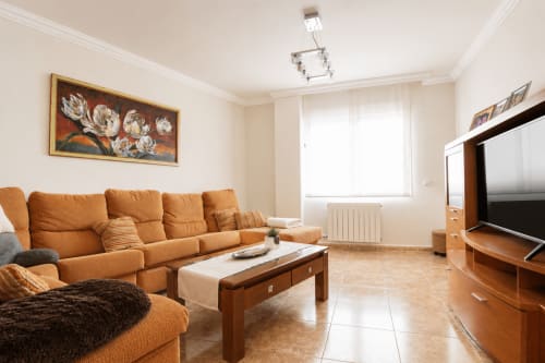 Luminoso salón de Riurau Home en Calp con sofá naranja, mueble TV de madera y equipamiento moderno