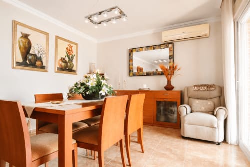 Zona de comedor del apartamento Quintanes en Riurau Home, Calp con mesa de madera naranja, sillas, televisor y butaca beige