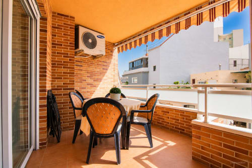 Soleado balcón en Riurau Home Calp con sillas naranjas, muros de ladrillo y vistas al mar Mediterráneo
