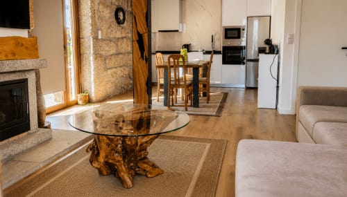Interior em open-plan da casa de campo com mesa de madeira, lareira, cozinha e vista para o lago na Casa Serração Gerês