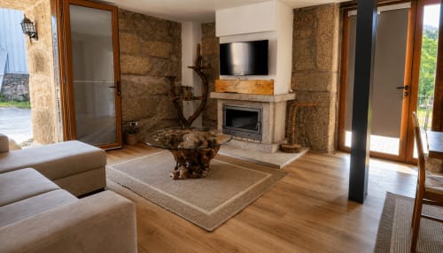 Sala de estar moderna com paredes de pedra, lareira, TV, assoalho de madeira e vista para o lago na casa de hóspedes Serração Gerês